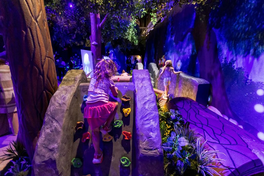 A young girl is climbing a rock wall in a play area, enjoying The Smurf Experience, a kid-friendly attraction in Dallas.
