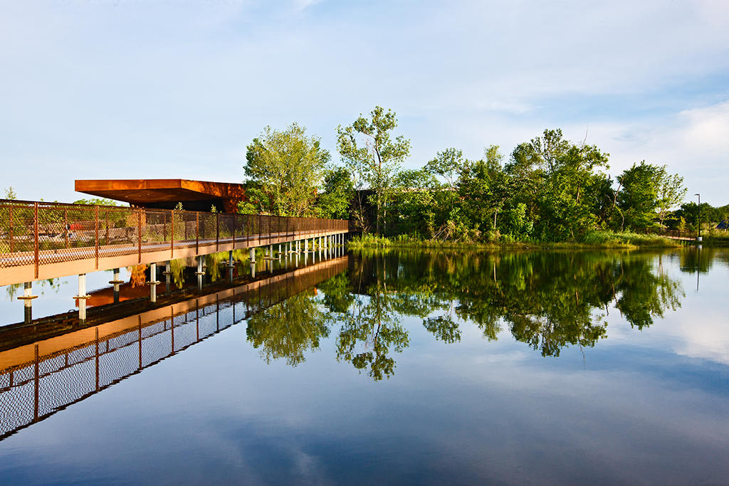 A scenic view of the Trinity River Audubon Center in Dallas, featuring lush greenery, walking trails, and families exploring nature — a top kid-friendly activity this August.